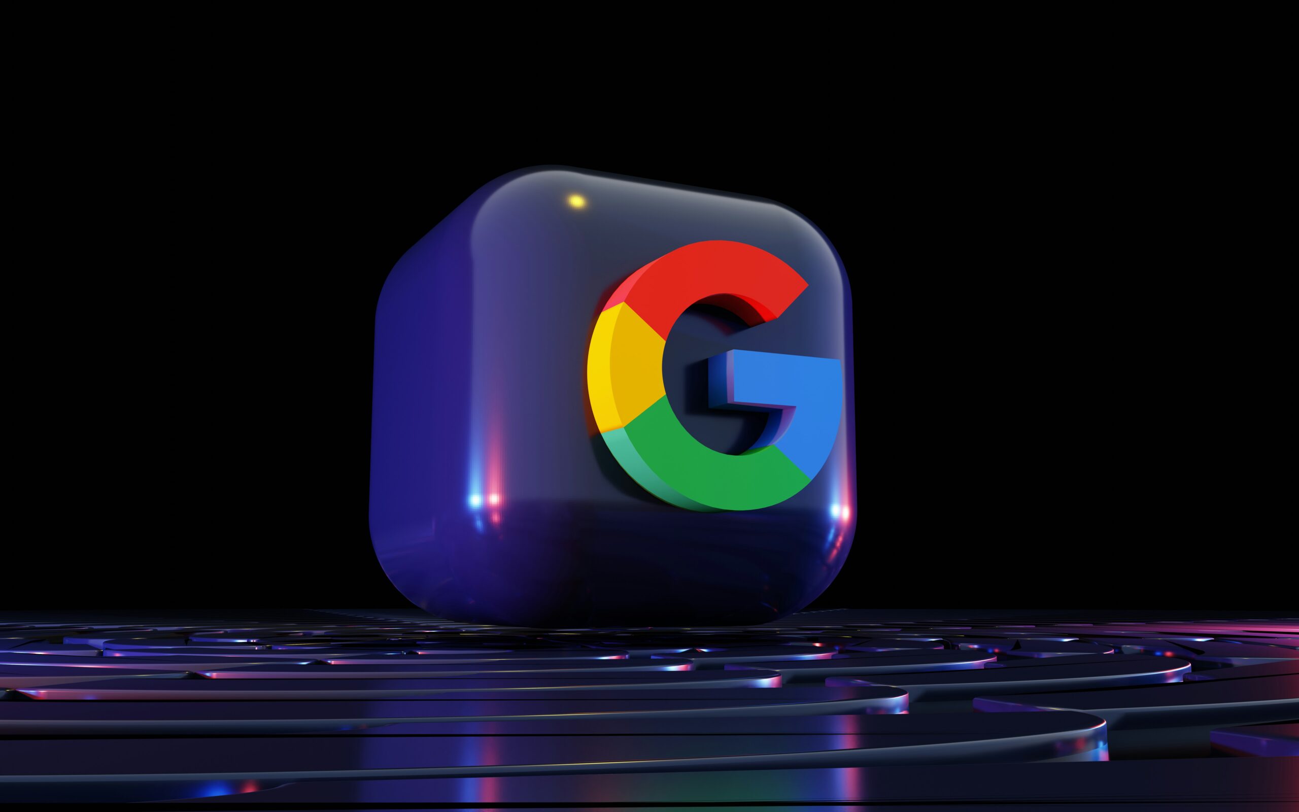 Un cubo negro en 3D con el logotipo de Google "G" en rojo, azul, amarillo y verde se asienta sobre una superficie futurista reflectante sobre un fondo oscuro.