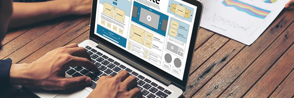 En una mesa de madera, una persona utiliza un portátil para diseñar una página web para una agencia de marketing, mientras otra revisa un gráfico de datos impreso.