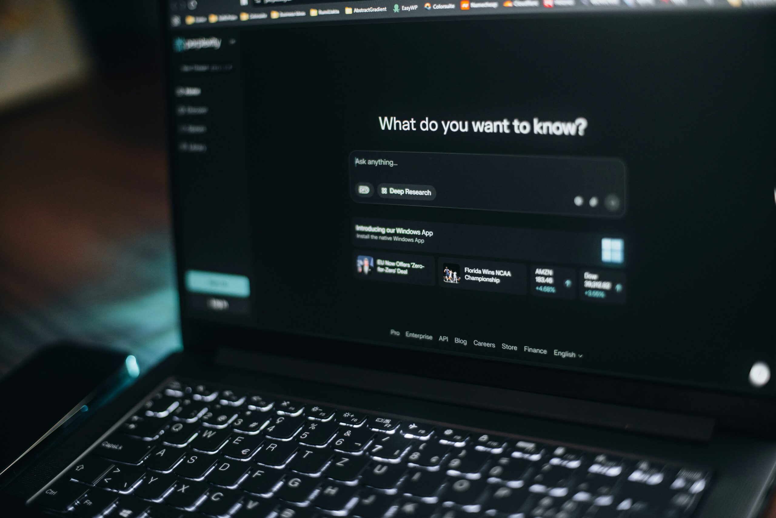 La pantalla de un portátil muestra una interfaz de chatbot de IA con una barra de búsqueda y temas sugeridos sobre un fondo de temática oscura.