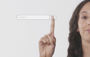 Una mujer señala con su dedo índice una barra de búsqueda virtual con el icono de una lupa sobre un fondo liso.