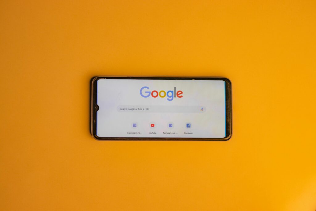 Sobre una superficie lisa de color naranja se encuentra un smartphone que muestra en su pantalla la página de inicio de la búsqueda de Google.