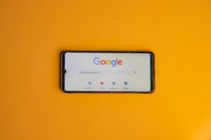 Sobre una superficie lisa de color naranja se encuentra un smartphone que muestra en su pantalla la página de inicio de la búsqueda de Google.