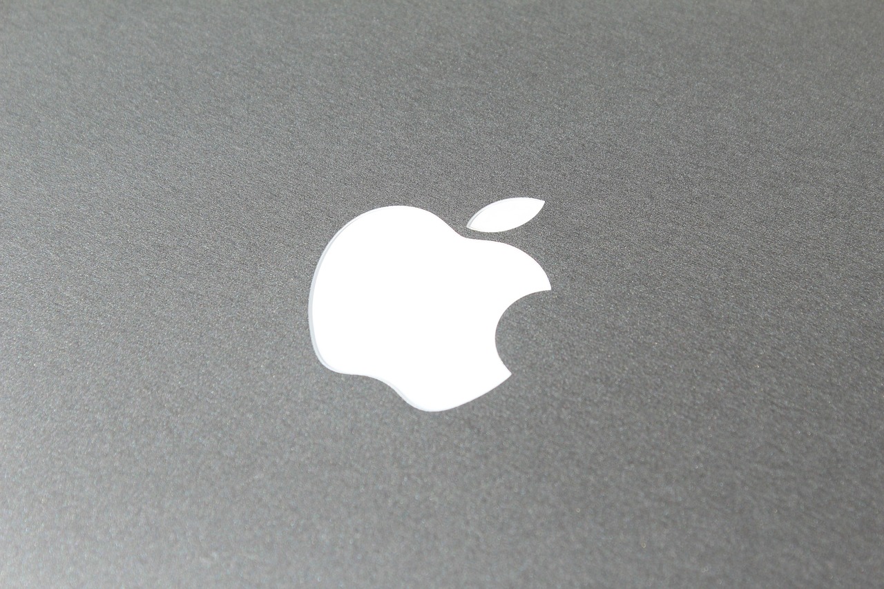Primer plano de un logotipo de Apple blanco sobre una superficie gris metálica.