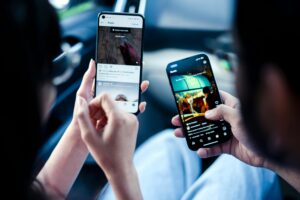 Dos personas sentadas una al lado de la otra, cada una con un smartphone en la mano y desplazándose por las aplicaciones de las redes sociales dentro de un coche.