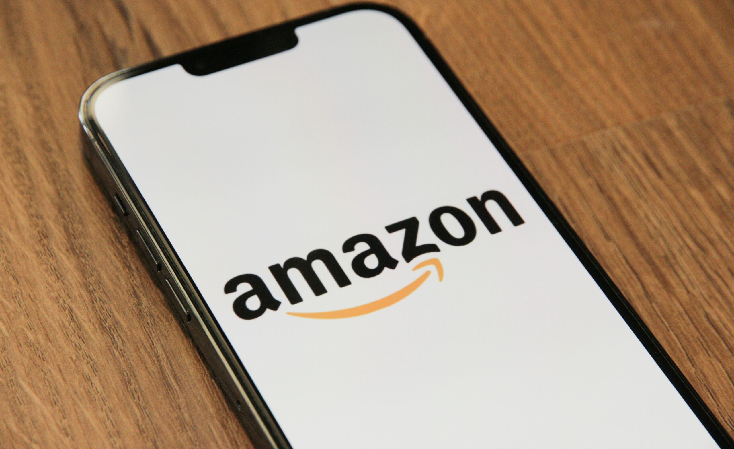 Un smartphone muestra el logotipo de Amazon en su pantalla mientras descansa sobre una superficie de madera.