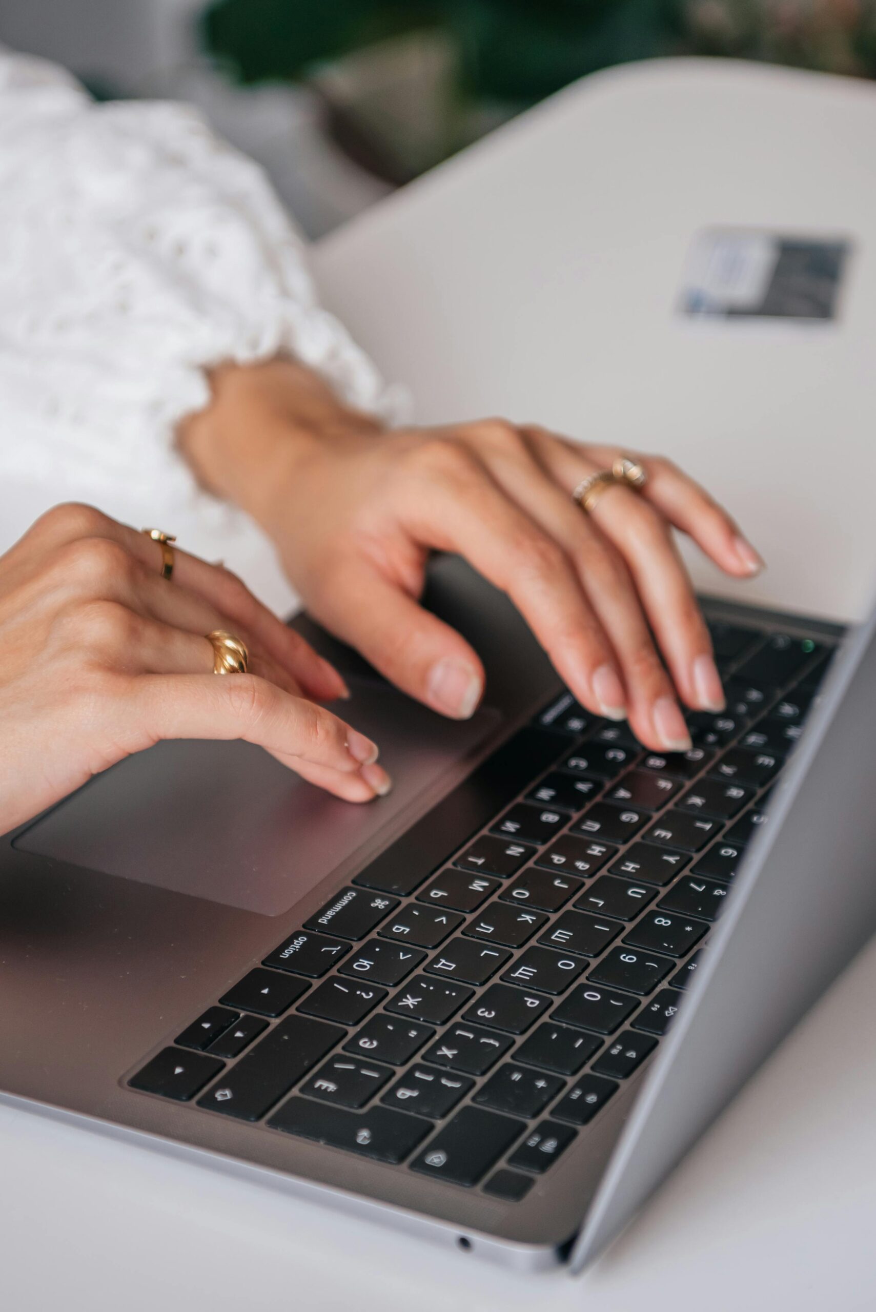 Primer plano de unas manos escribiendo en el teclado de un ordenador portátil, con una funda blanca visible y una tarjeta de crédito al fondo.