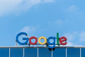 Logotipo de Google en letras de colores en la parte superior de un edificio de cristal contra un cielo azul con algunas nubes.