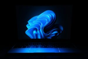 Un ordenador portátil con un diseño abstracto azul brillante en su pantalla en un entorno oscuro.