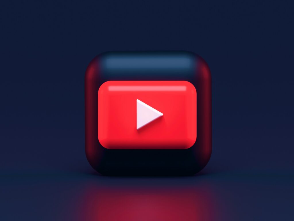 Un botón 3D cuadrado rojo y negro con un icono de reproducción blanco, parecido al logotipo de YouTube, está centrado sobre un fondo azul oscuro.