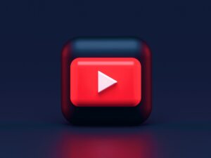 Un botón 3D cuadrado rojo y negro con un icono de reproducción blanco, parecido al logotipo de YouTube, está centrado sobre un fondo azul oscuro.