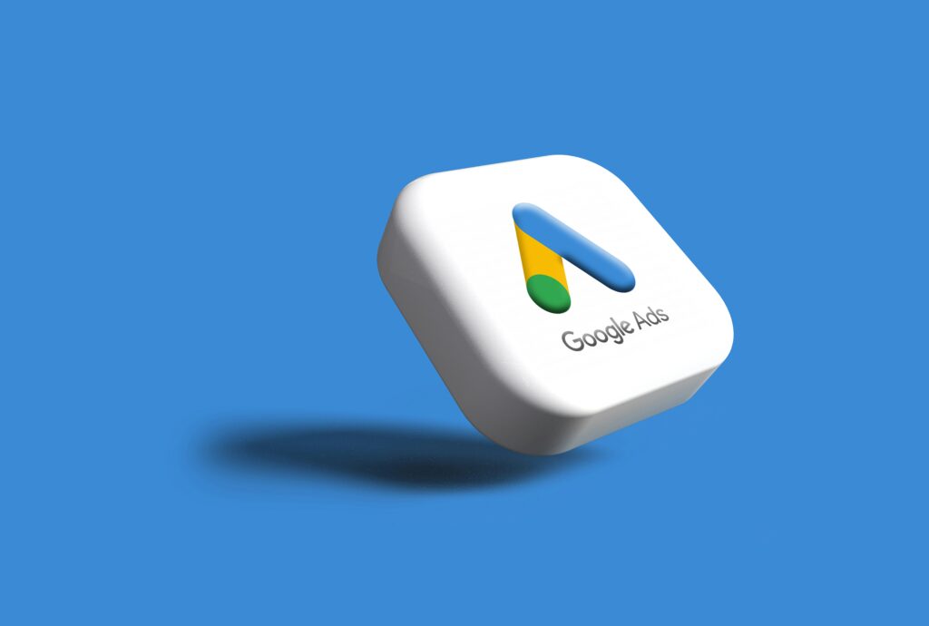 Un icono cuadrado en 3D con el logotipo de Google Ads y el texto "Google Ads" flota sobre un fondo azul sólido, proyectando una sombra debajo.