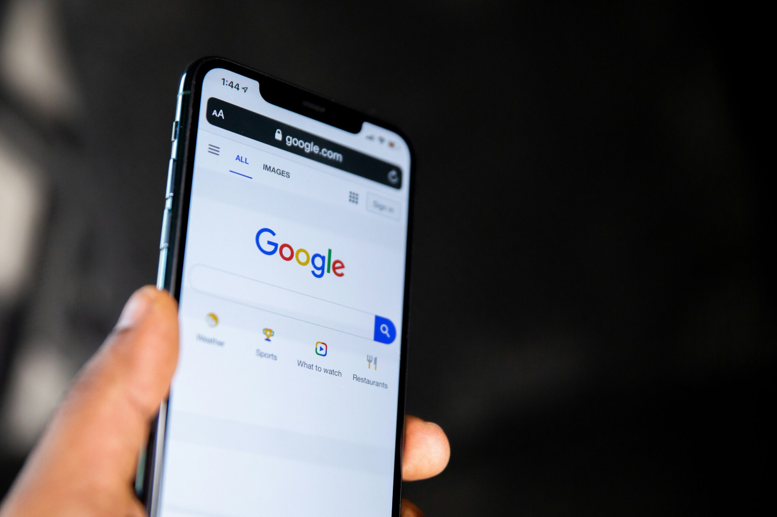 Una persona sostiene un smartphone que muestra la página de inicio de búsqueda de Google, con la barra de búsqueda visible en la pantalla.