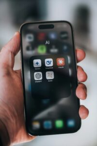 Una mano sostiene un teléfono inteligente que muestra una carpeta llamada "AI" con aplicaciones: Gemini, DeepSeek, Claude, ChatGPT y Auren en la pantalla.