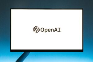 Un monitor muestra el logotipo de OpenAI y la palabra "OpenAI" sobre un fondo blanco liso.