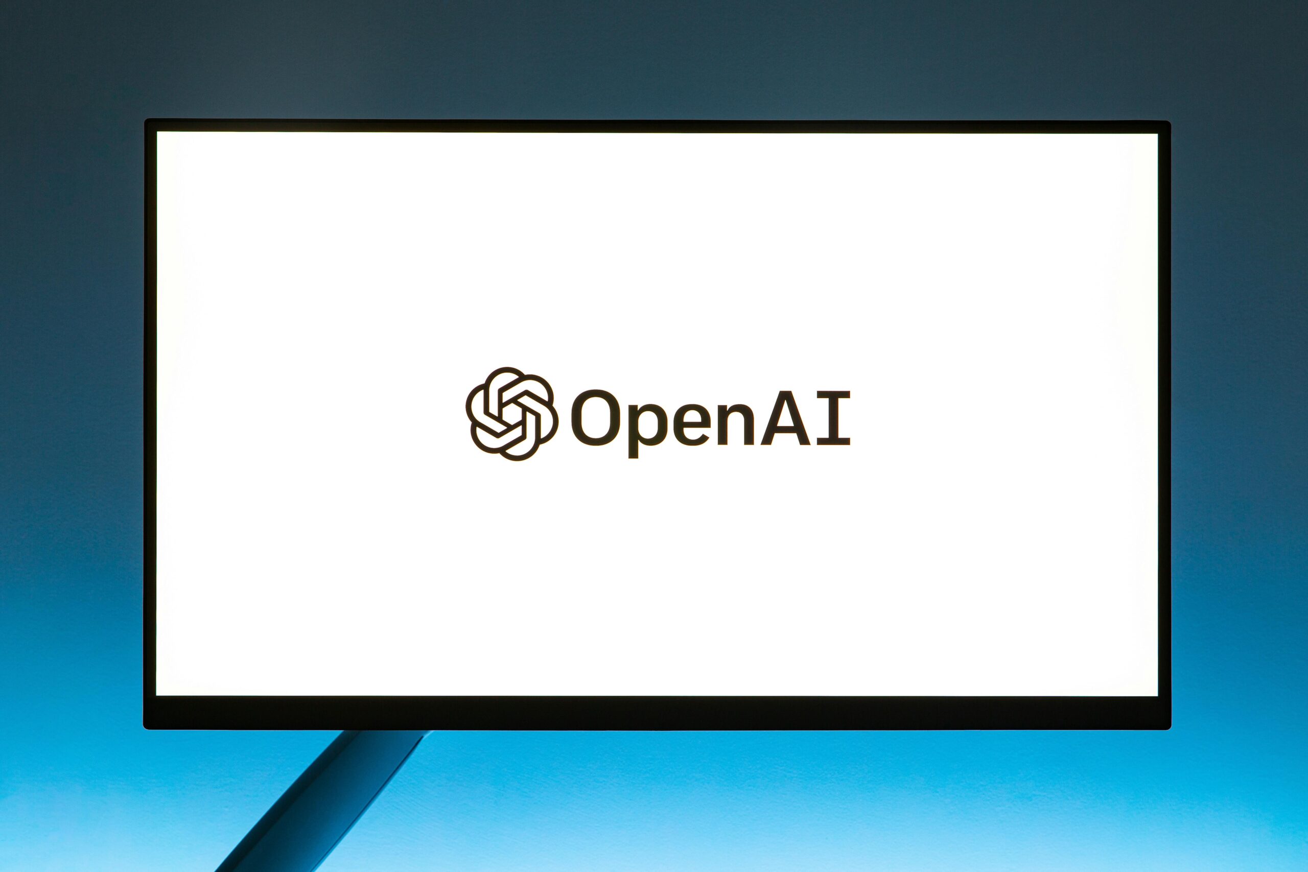 Un monitor muestra el logotipo de OpenAI y la palabra "OpenAI" sobre un fondo blanco liso.