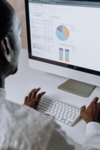 Persona que trabaja con un ordenador mostrando hojas de cálculo y gráficos, incluidos un gráfico circular y gráficos de barras, en un monitor de gran tamaño.