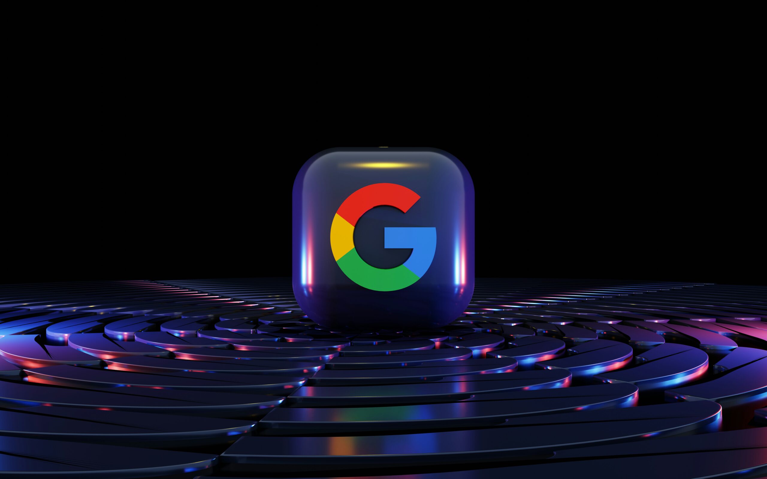 Un cubo en 3D con el logotipo de Google se asienta sobre una superficie circular concéntrica brillante sobre un fondo negro, iluminado por luces de colores.