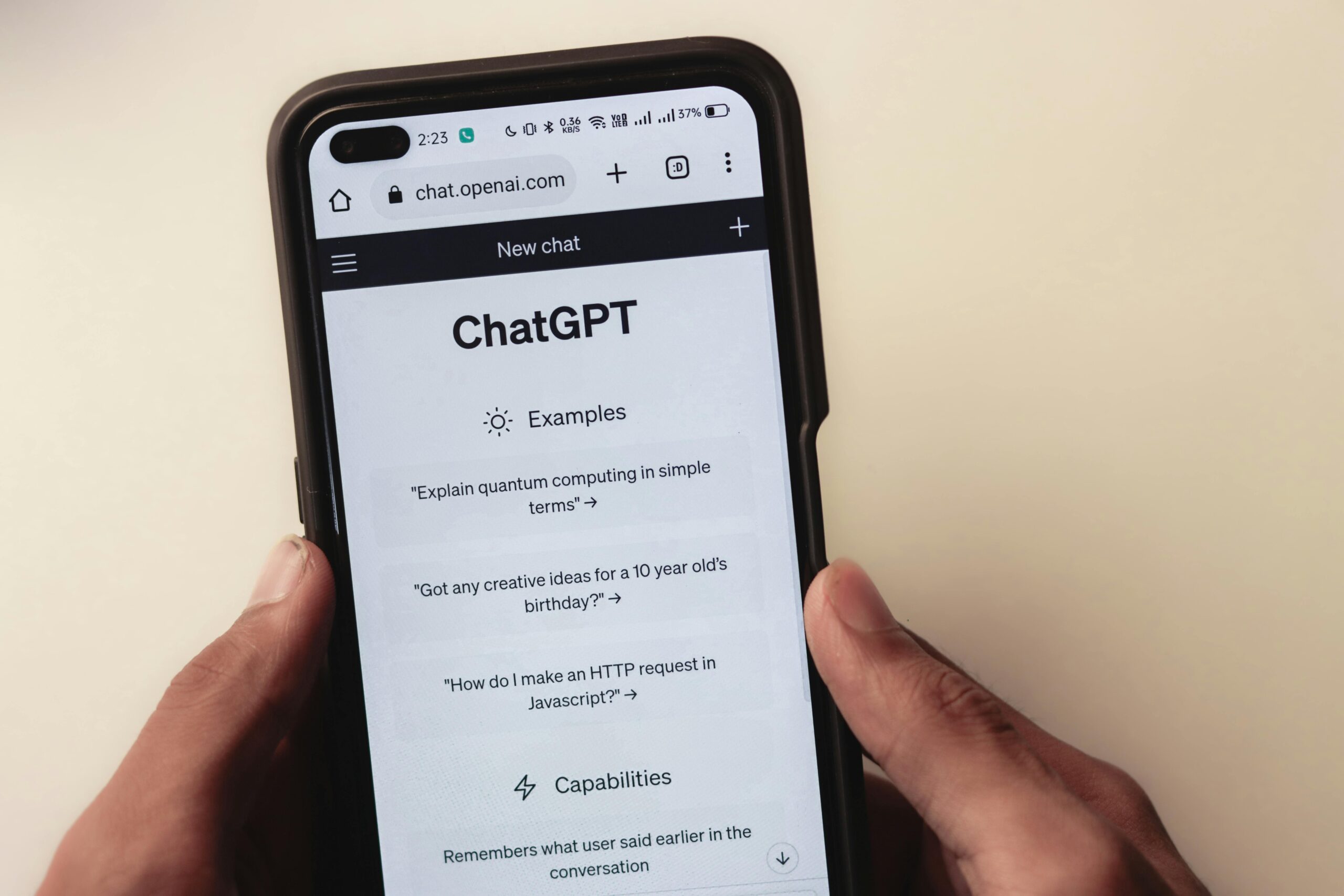 Una persona sostiene un smartphone en el que aparece el sitio web ChatGPT, mostrando en la pantalla mensajes de ejemplo y funciones.
