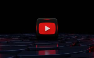 Un icono en 3D del botón de reproducción de YouTube se sitúa en una plataforma circular oscura y brillante sobre un fondo negro.