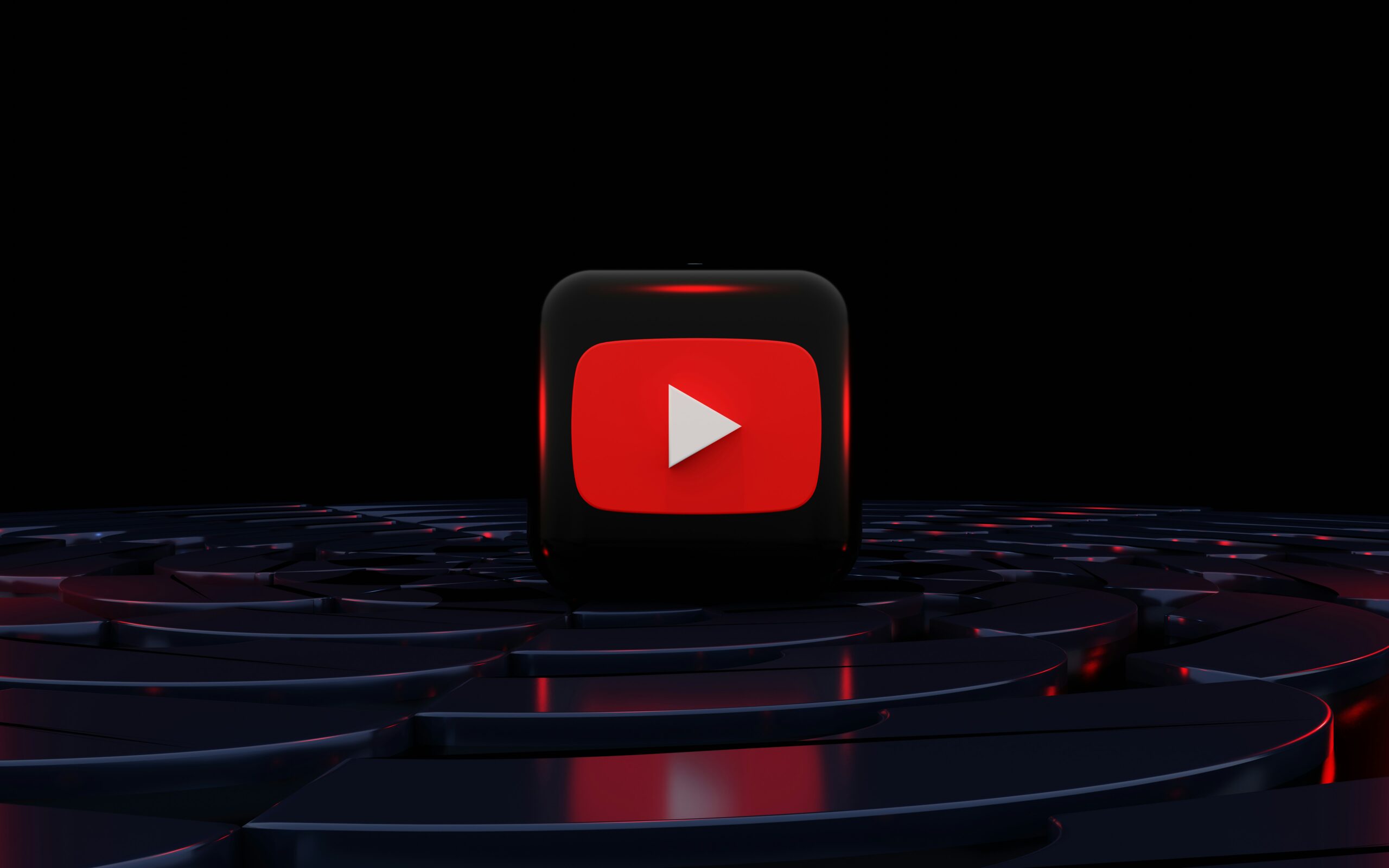 Un icono en 3D del botón de reproducción de YouTube se sitúa en una plataforma circular oscura y brillante sobre un fondo negro.
