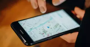Una persona utiliza un smartphone que muestra una aplicación de mapas digitales, con los dedos posados sobre la pantalla, buscando destacar frente a tu competencia mediante SEO local avanzado y búsquedas de última hora.