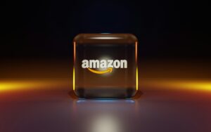 Un cubo de cristal con el logotipo de Amazon y una flecha amarilla aparece sobre una superficie reflectante con un fondo degradado oscuro.