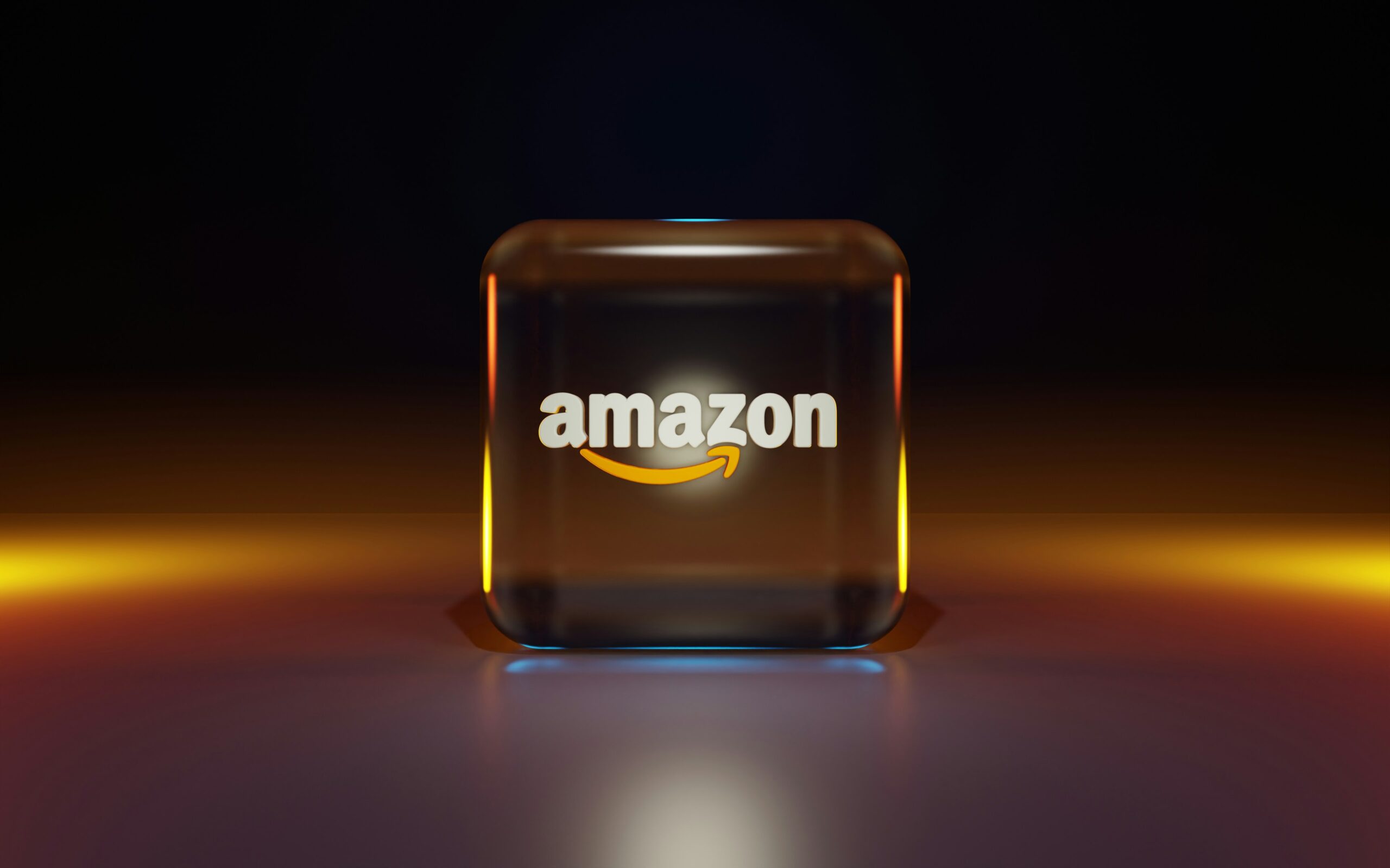 Un cubo de cristal con el logotipo de Amazon y una flecha amarilla aparece sobre una superficie reflectante con un fondo degradado oscuro.