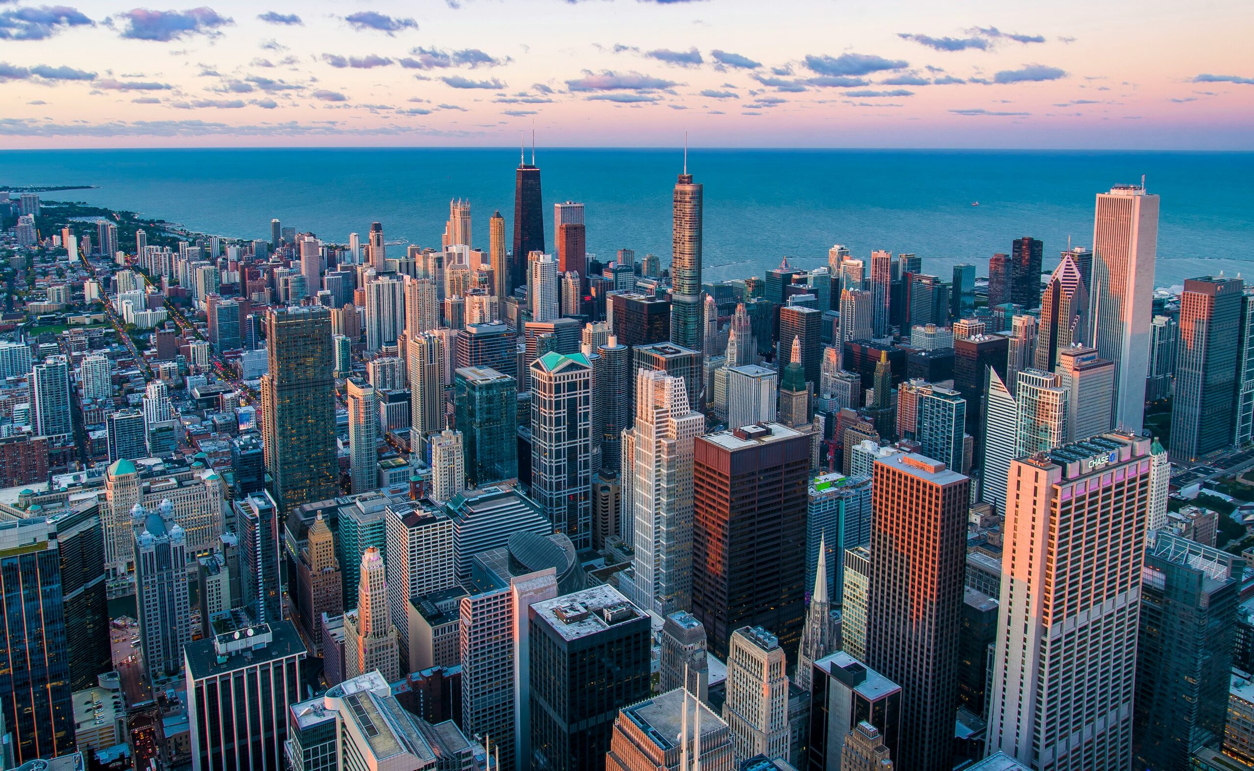 Vista aérea de los rascacielos del centro de Chicago con el lago Michigan de fondo bajo un cielo parcialmente nublado al atardecer.