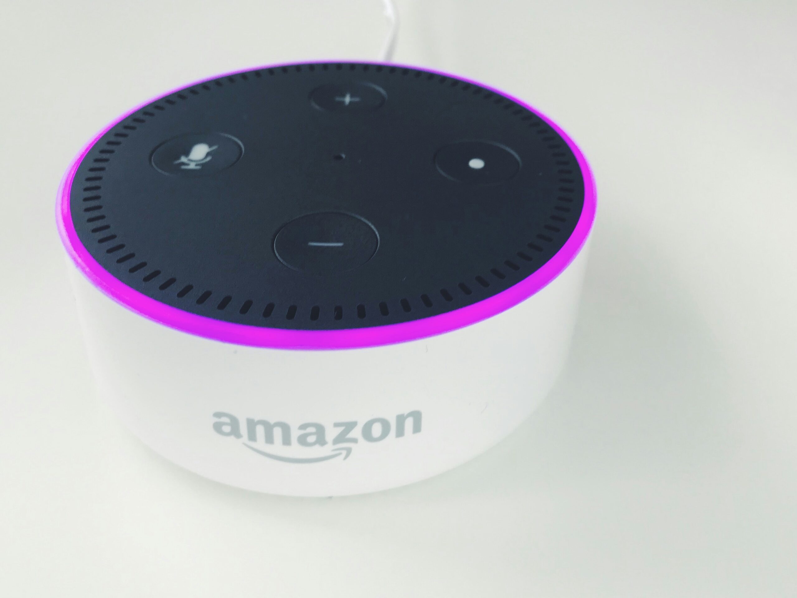 Un altavoz inteligente Amazon Echo Dot blanco con la parte superior negra y un anillo luminoso morado se asienta sobre una superficie blanca.