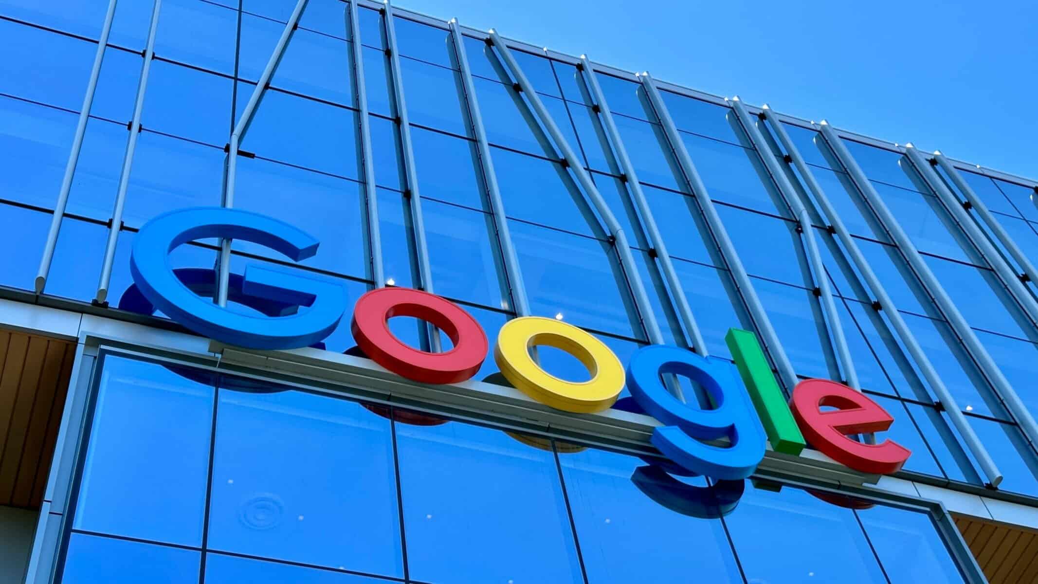 El logotipo de Google aparece en el exterior de un moderno edificio de cristal bajo un cielo azul despejado.