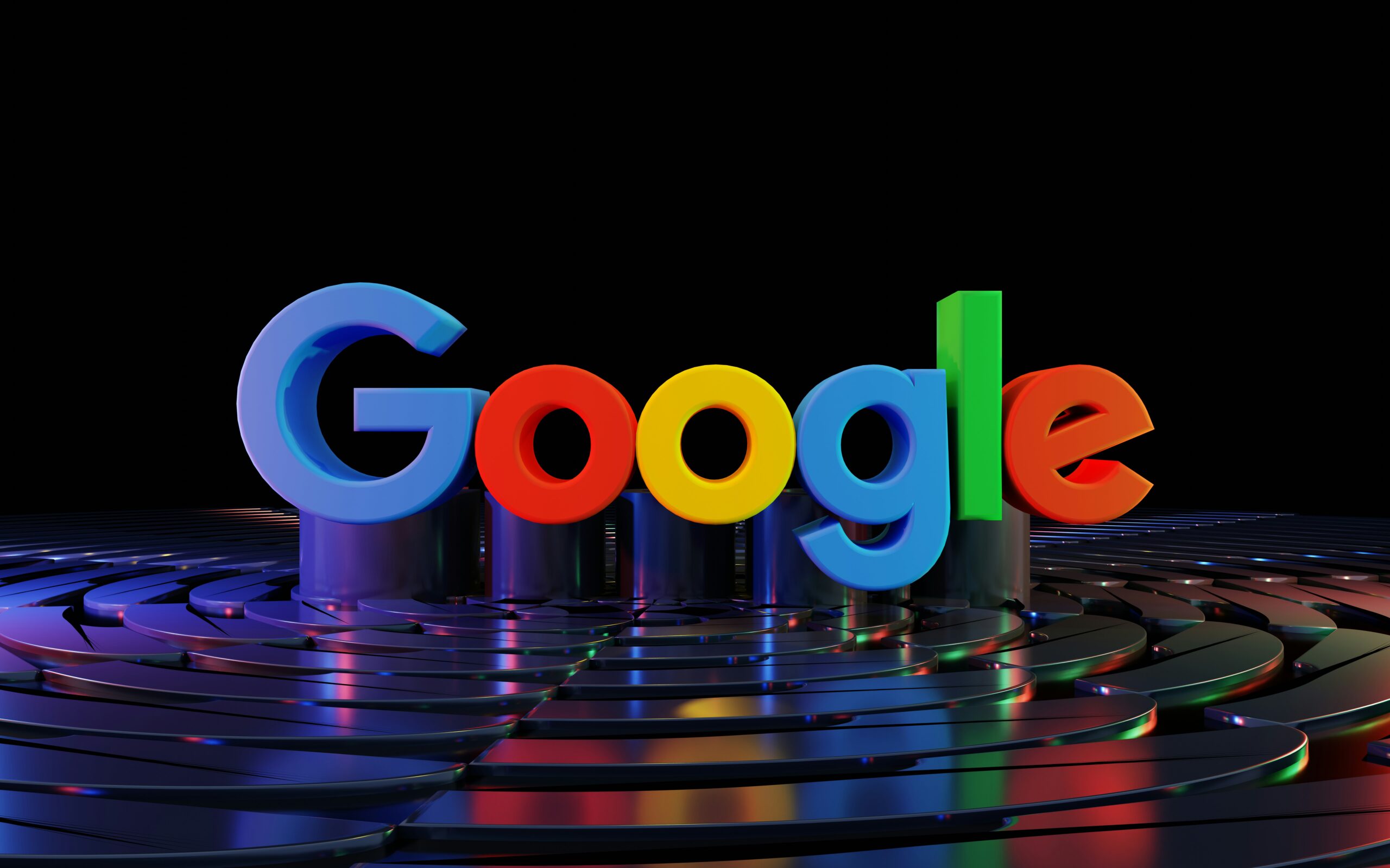 El logotipo de Google en coloridas letras 3D se alza sobre una superficie reflectante con motivos curvos y metálicos y un fondo negro.