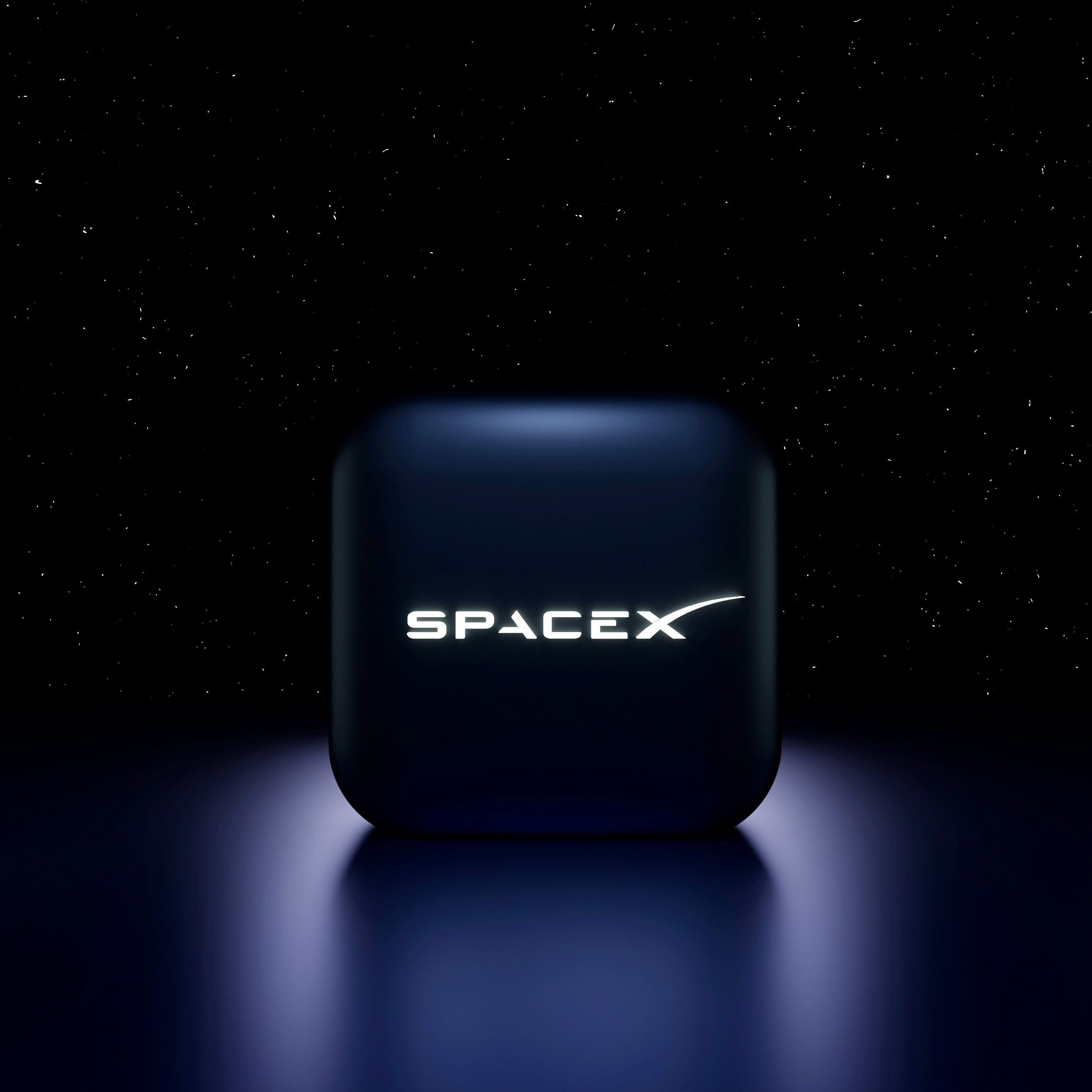 Un cubo negro con el logotipo de SpaceX iluminado en su parte frontal se asienta sobre una superficie reflectante sobre un fondo de cielo nocturno estrellado.
