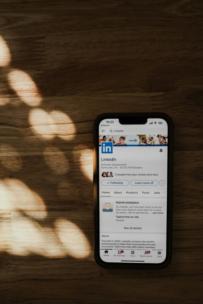 Un smartphone que muestra la página del perfil de empresa de LinkedIn descansa sobre una superficie de madera a la que llega la luz del sol.