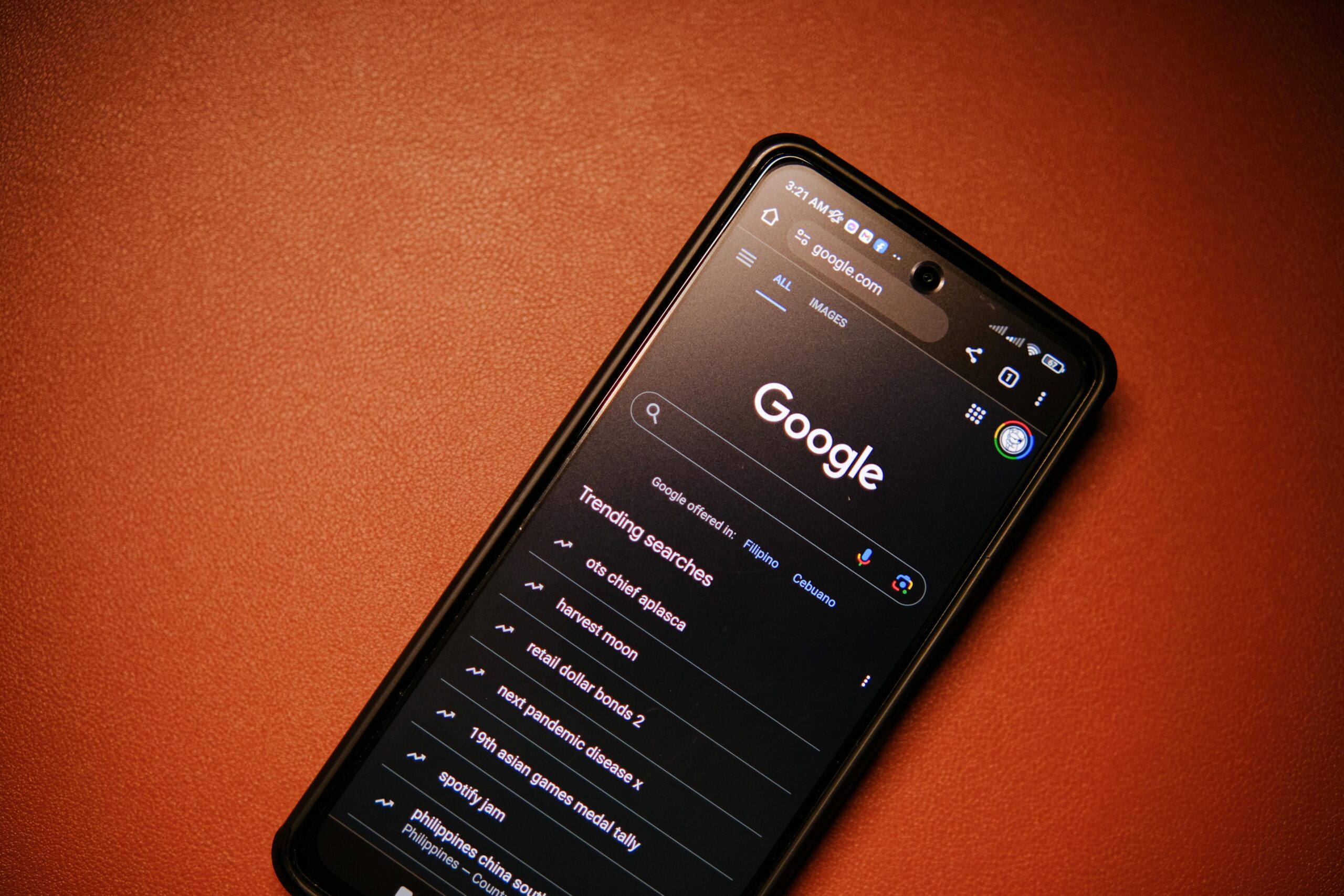 Un smartphone con una página de búsqueda de Google de temática oscura abierta, que muestra las búsquedas de tendencias, descansa sobre una superficie marrón.