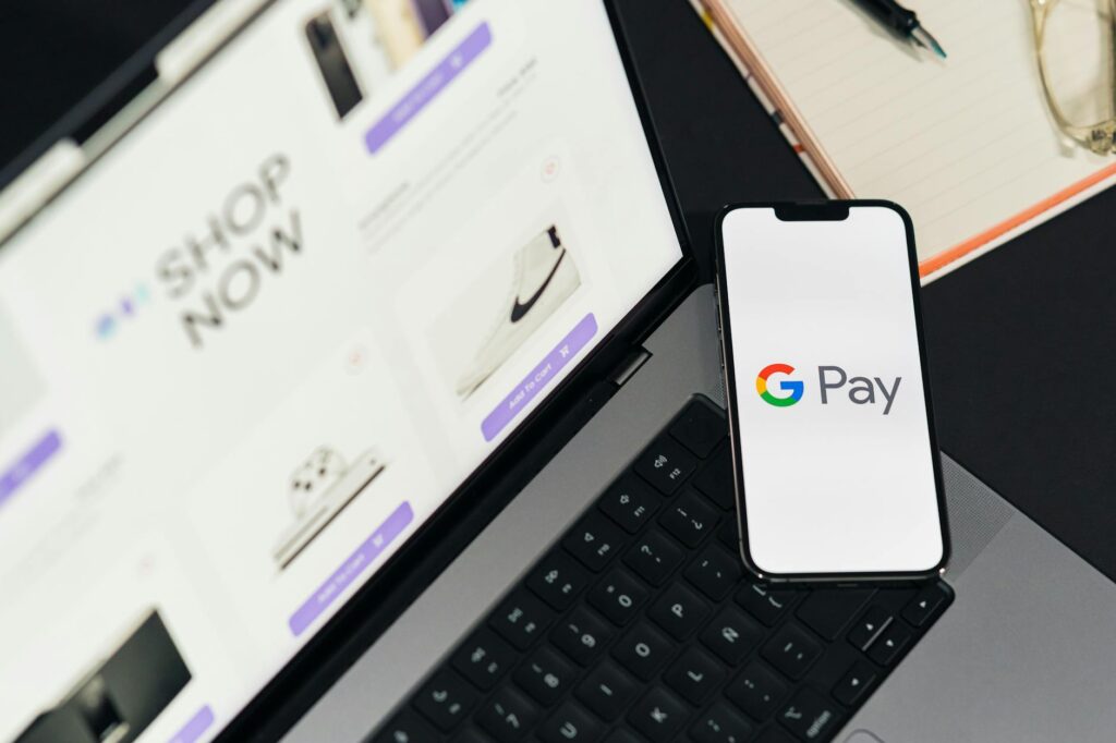 Inicio 14 Un smartphone con el logotipo de Google Pay descansa sobre el teclado de un portátil, con un sitio web de compras online abierto en la pantalla del portátil.