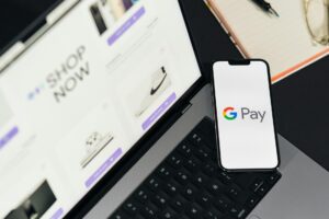 Un smartphone con el logotipo de Google Pay descansa sobre el teclado de un portátil, con un sitio web de compras online abierto en la pantalla del portátil.