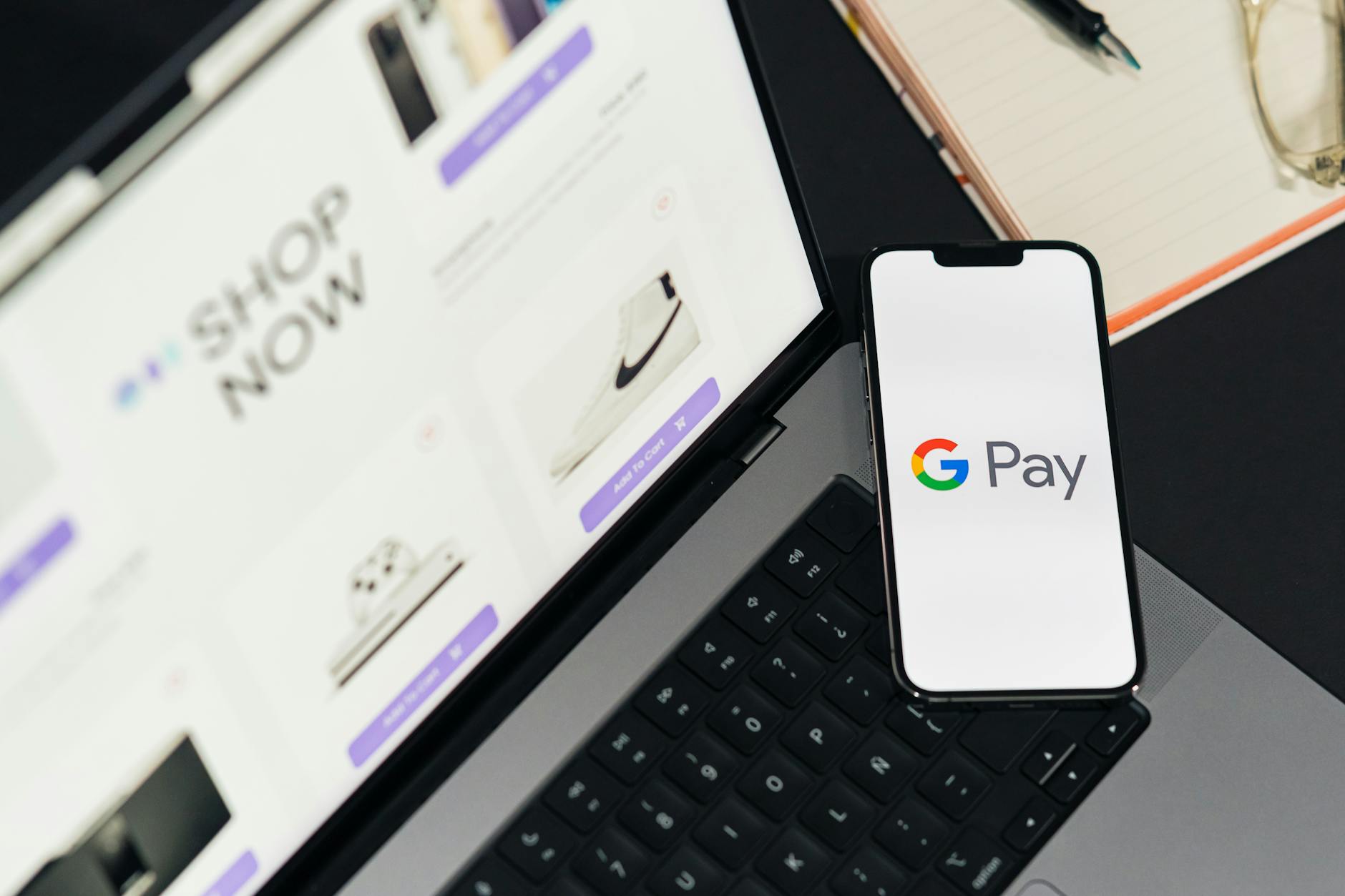 Un smartphone con el logotipo de Google Pay descansa sobre el teclado de un portátil, con un sitio web de compras online abierto en la pantalla del portátil.