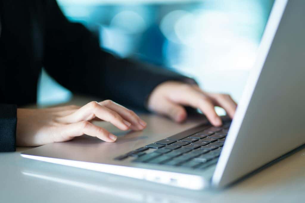Una persona escribe en el teclado de un ordenador portátil, con las manos enfocadas y el fondo borroso.