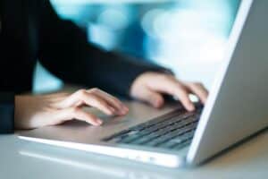 Una persona escribe en el teclado de un ordenador portátil, con las manos enfocadas y el fondo borroso.