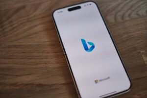 Un smartphone muestra el logotipo de Bing en su pantalla, con un pequeño logotipo de Microsoft en la parte inferior, colocado sobre una superficie de madera.