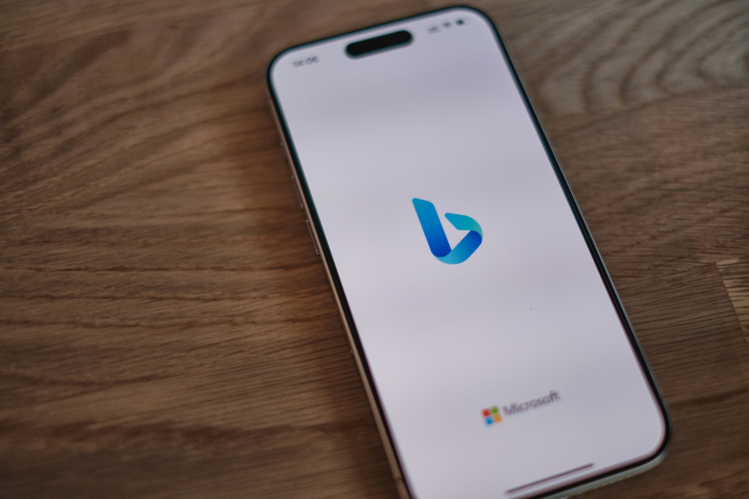 Un smartphone muestra el logotipo de Bing en su pantalla, con un pequeño logotipo de Microsoft en la parte inferior, colocado sobre una superficie de madera.