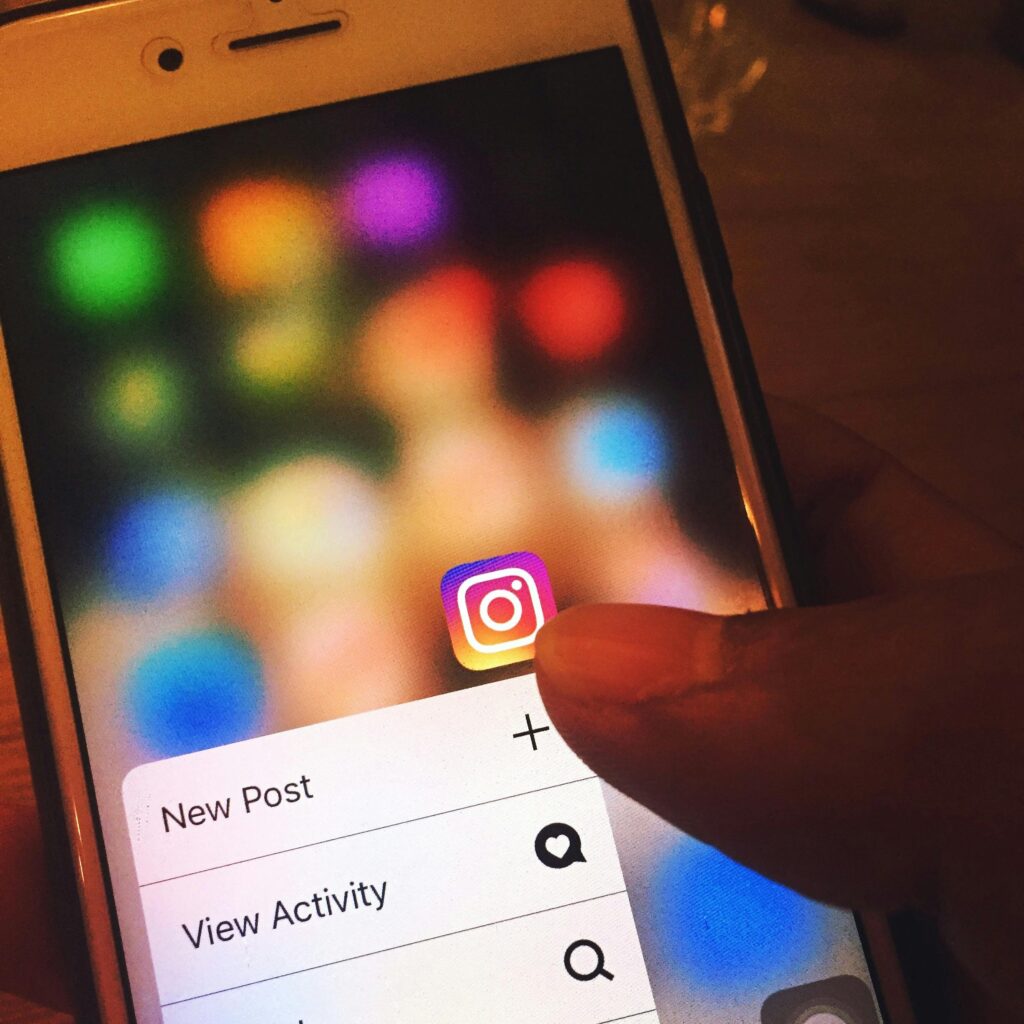 Una mano sujeta un smartphone que muestra el icono de la aplicación Instagram con las opciones "Nueva publicación" y "Ver actividad" en la pantalla.