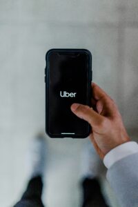 Una persona sostiene un smartphone en cuya pantalla aparece el logotipo de la aplicación Uber, visto desde arriba sobre un fondo borroso.