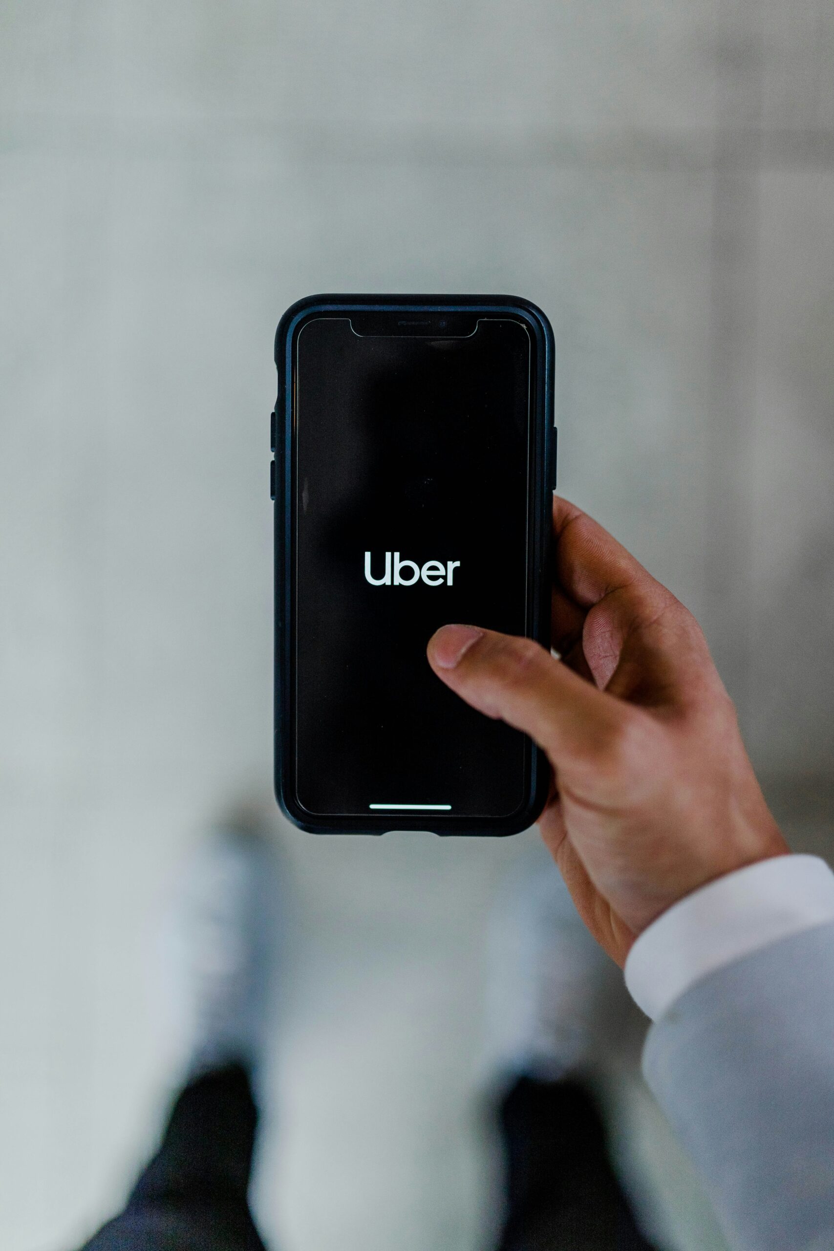 Una persona sostiene un smartphone en cuya pantalla aparece el logotipo de la aplicación Uber, visto desde arriba sobre un fondo borroso.