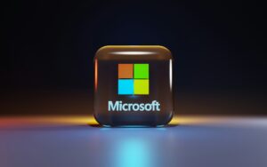 Icono en 3D del logotipo de Microsoft con cuatro cuadrados de colores y la palabra "Microsoft" debajo, sobre un fondo brillante y oscuro.